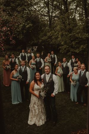 Wedding party in sage green and gray attire posed in forest setting.