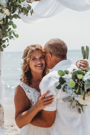 A beachside wedding scene with white floral decorations and ocean waves in the background.