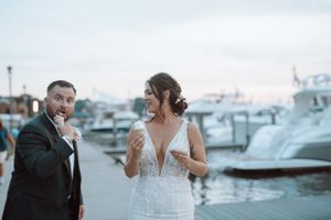 A playful wedding moment by a marina with boats in the background.