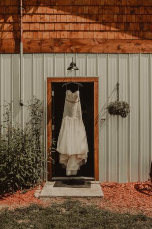 White wedding dress hanging in a wooden doorframe against corrugated metal siding at dusk.