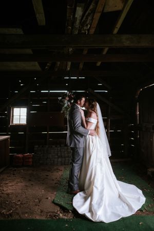 Romantic wedding couple shares an intimate moment in a rustic barn with streaming light.