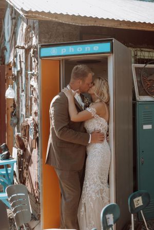 Intimate moment between couple in front of vintage phone booth with rustic decor.