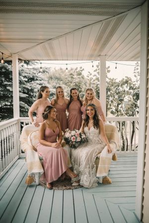 Bridal party in pink dresses poses together on a white wooden porch.