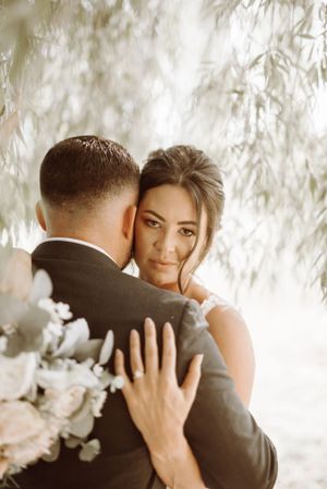 Intimate wedding moment captured through willow branches with soft lighting.