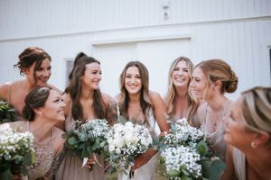 Candid moment of bridesmaids laughing together while holding white floral bouquets.