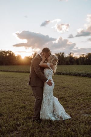 A romantic sunset wedding photo of a couple embracing in an open field.
