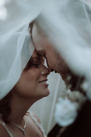 Intimate moment captured under flowing white wedding veil in soft lighting.