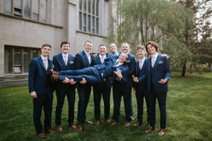 Groomsmen in navy suits posing together on lawn outside building.