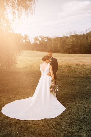 Bride in flowing white dress with long train during golden hour sunset photo.