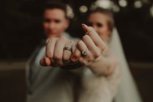 Close up photo of wedding rings being displayed on hands against a dark background.