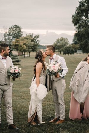 Wedding party in light gray attire poses with bouquets on a grassy hillside.
