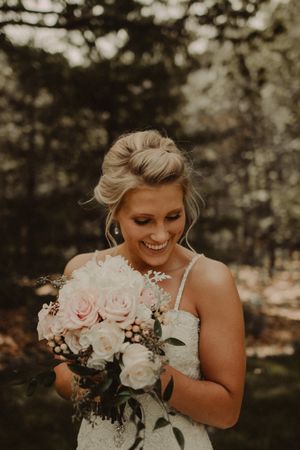 Bride holding blush pink and white rose bouquet in outdoor portrait.