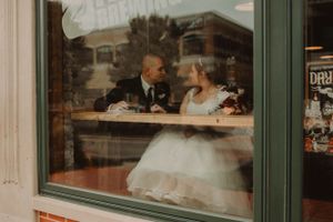 A wedding couple shares a tender moment through a cafe window.