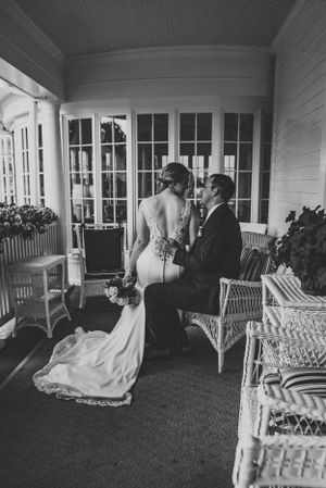 Classic black and white portrait of newlyweds on a elegant porch with wicker furniture.