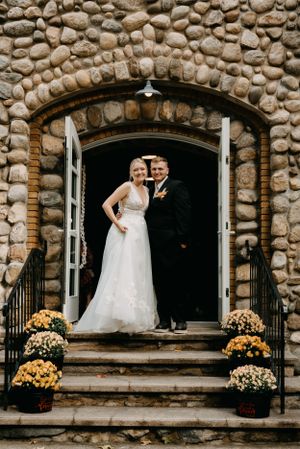 A wedding couple poses in an elegant stone archway decorated with yellow mums.