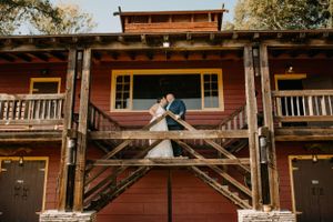 A romantic wedding portrait on the steps of a rustic red wooden building with vintage architecture.