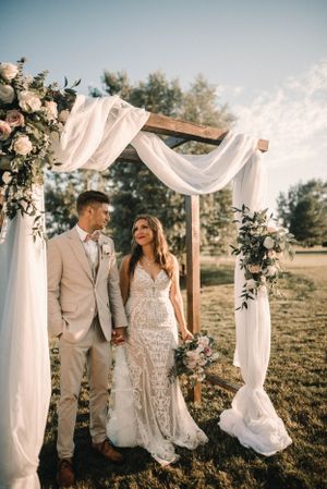 Wedding ceremony setup with white draped arch adorned with blush roses in an outdoor setting.
