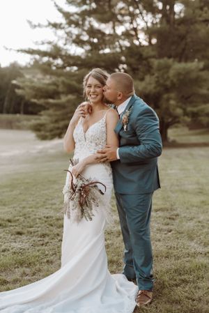 A tender moment between newlyweds in a garden setting with pine trees in the background.
