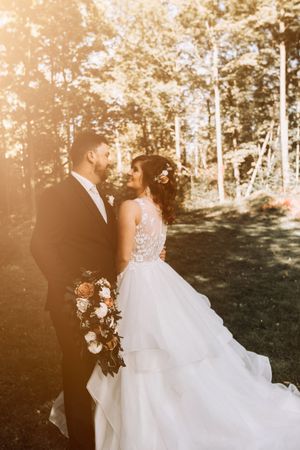 A sunlit wedding portrait featuring a couple holding a bouquet in a forest setting.