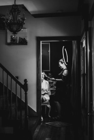 An artistic black and white photo captures wedding preparations in a dimly lit hallway.