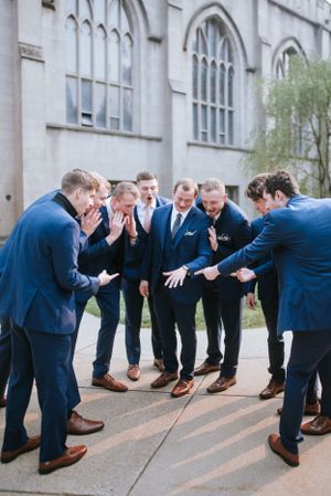 Groomsmen in navy suits huddled in a circle outside a gothic church building.