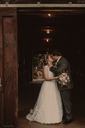 Moody wedding portrait in dark wooden tunnel lit by vintage ceiling lights.