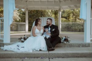 Couple sits with their dog under a white gazebo during their wedding celebration.