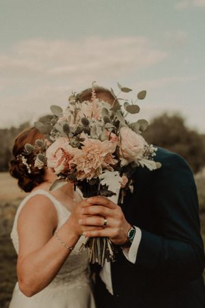 Pink and white bridal bouquet held between a couple during an intimate wedding moment at sunset.