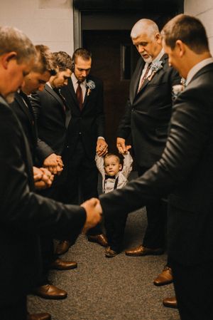 A touching moment of prayer with groomsmen gathered in suits around a small ring bearer.