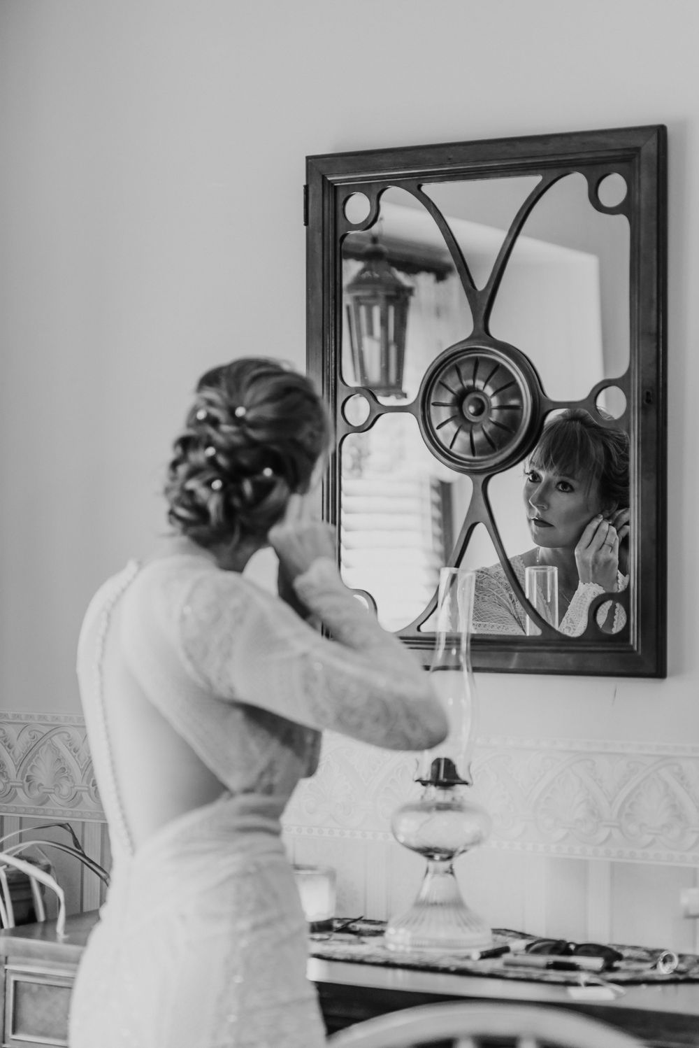 A bride prepares for her wedding day while looking into an ornate mirror with decorative metalwork.