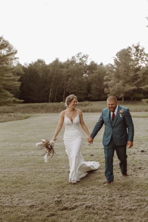 A couple walks hand in hand across a grassy field during their wedding.