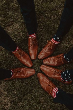 Circle of brown leather dress shoes with patriotic American flag socks on grass.