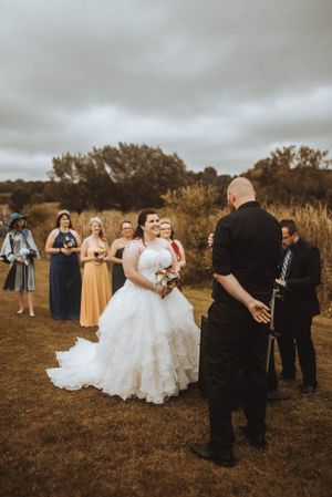 Outdoor wedding ceremony with bridal party in navy and yellow dresses on autumn day.