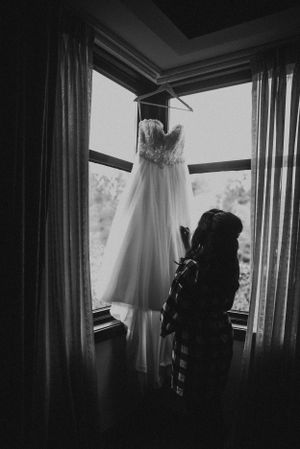 Wedding dress hanging in window silhouetted against natural light.