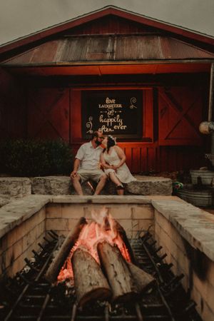 Rustic outdoor fireplace scene at a cabin with glowing logs burning in the foreground.