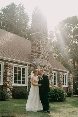 Wedding couple shares intimate moment by stone chimney of rustic house.