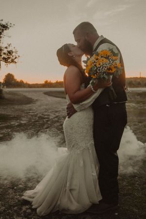 Sunset wedding portrait with couple embracing while holding sunflower bouquet.