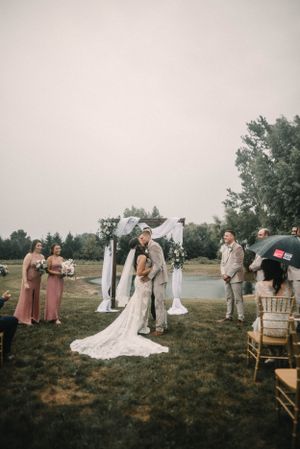 Outdoor wedding ceremony under white arch with guests seated on lawn.