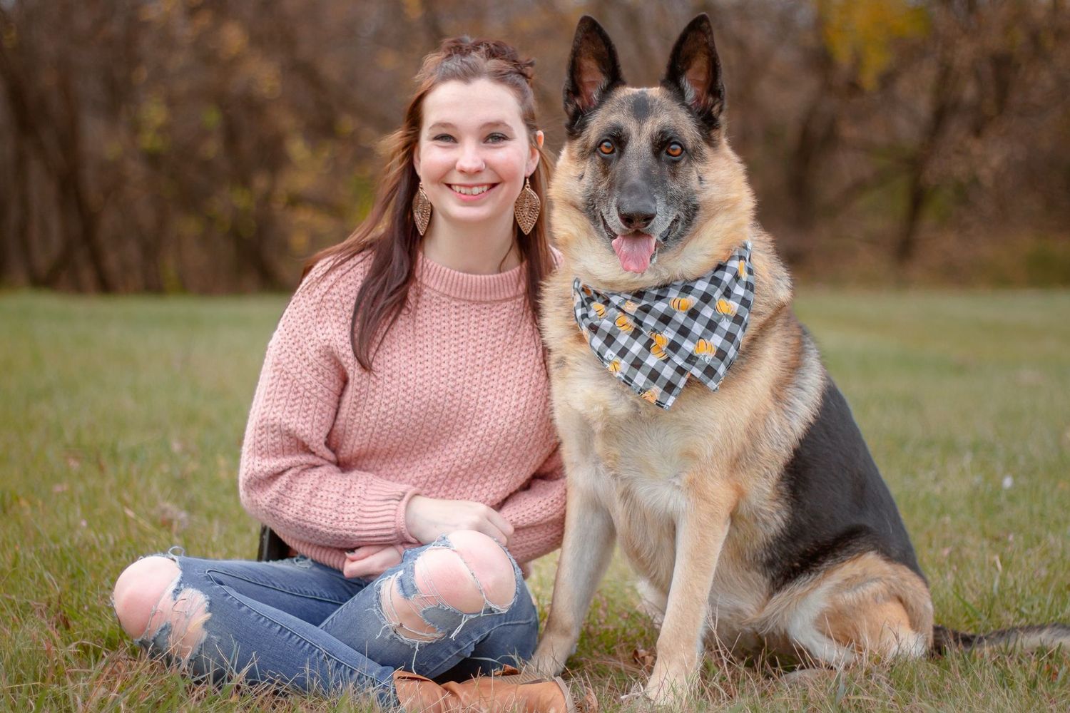 Person sitting in grass with friendly German Shepherd dog wearing bandana.
