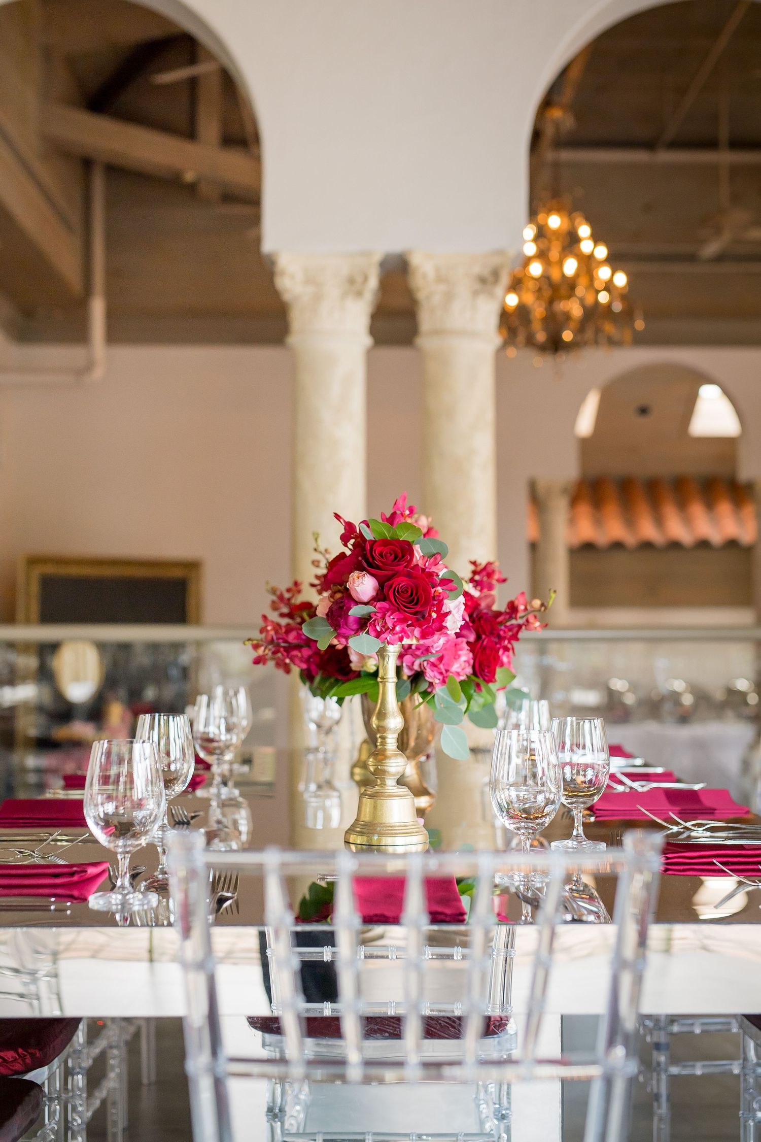 Luxurious table setting with pink floral centerpiece, crystal glasses and gold accents in an arched venue.
