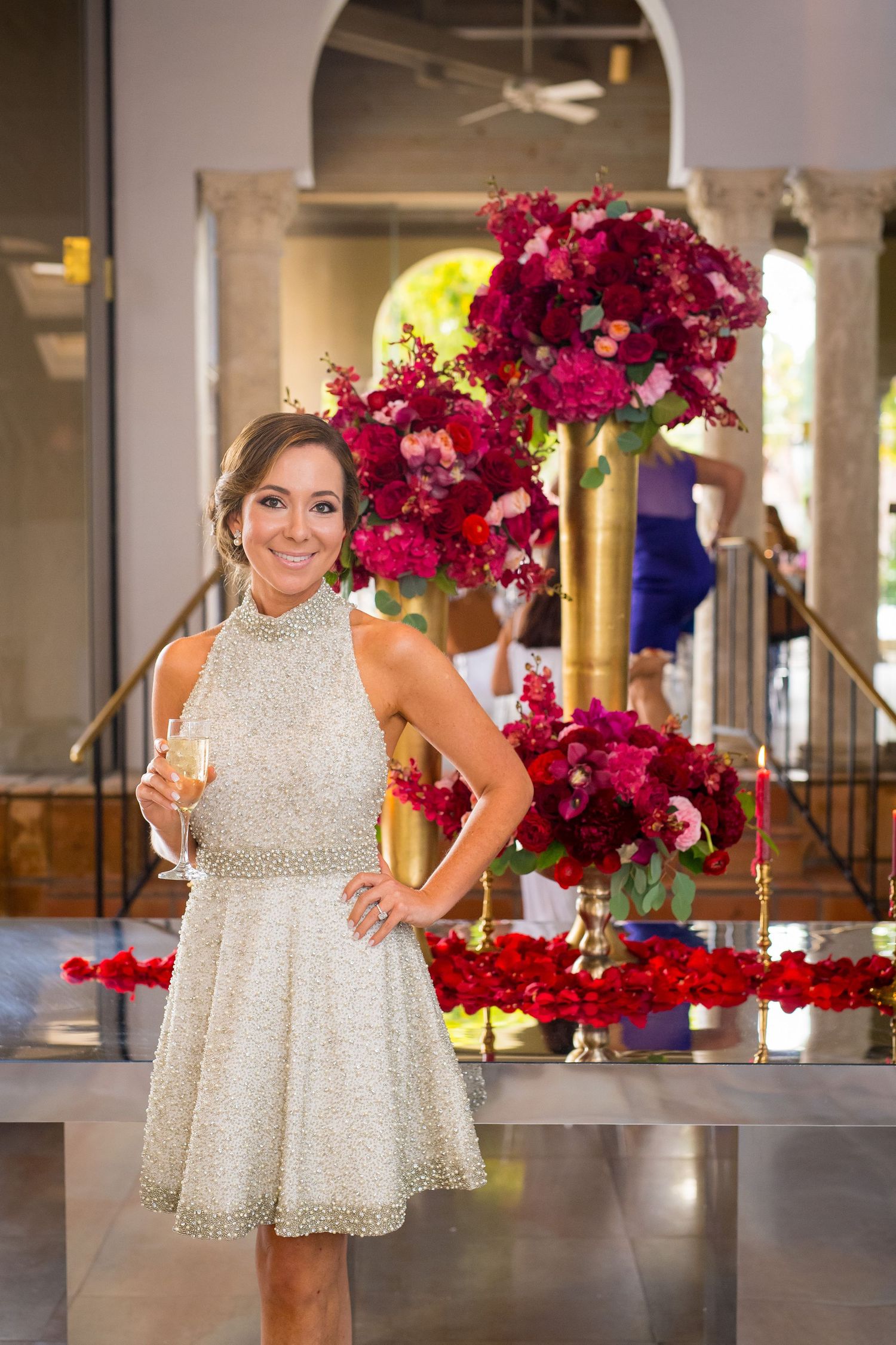 White dress against backdrop of pink floral arrangements and gold decor in elegant venue.