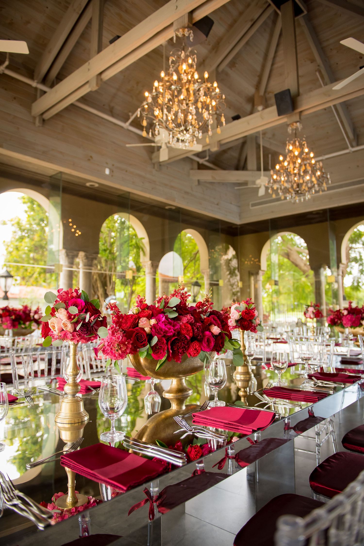 Luxurious wedding reception hall with crystal chandeliers and burgundy floral centerpieces.