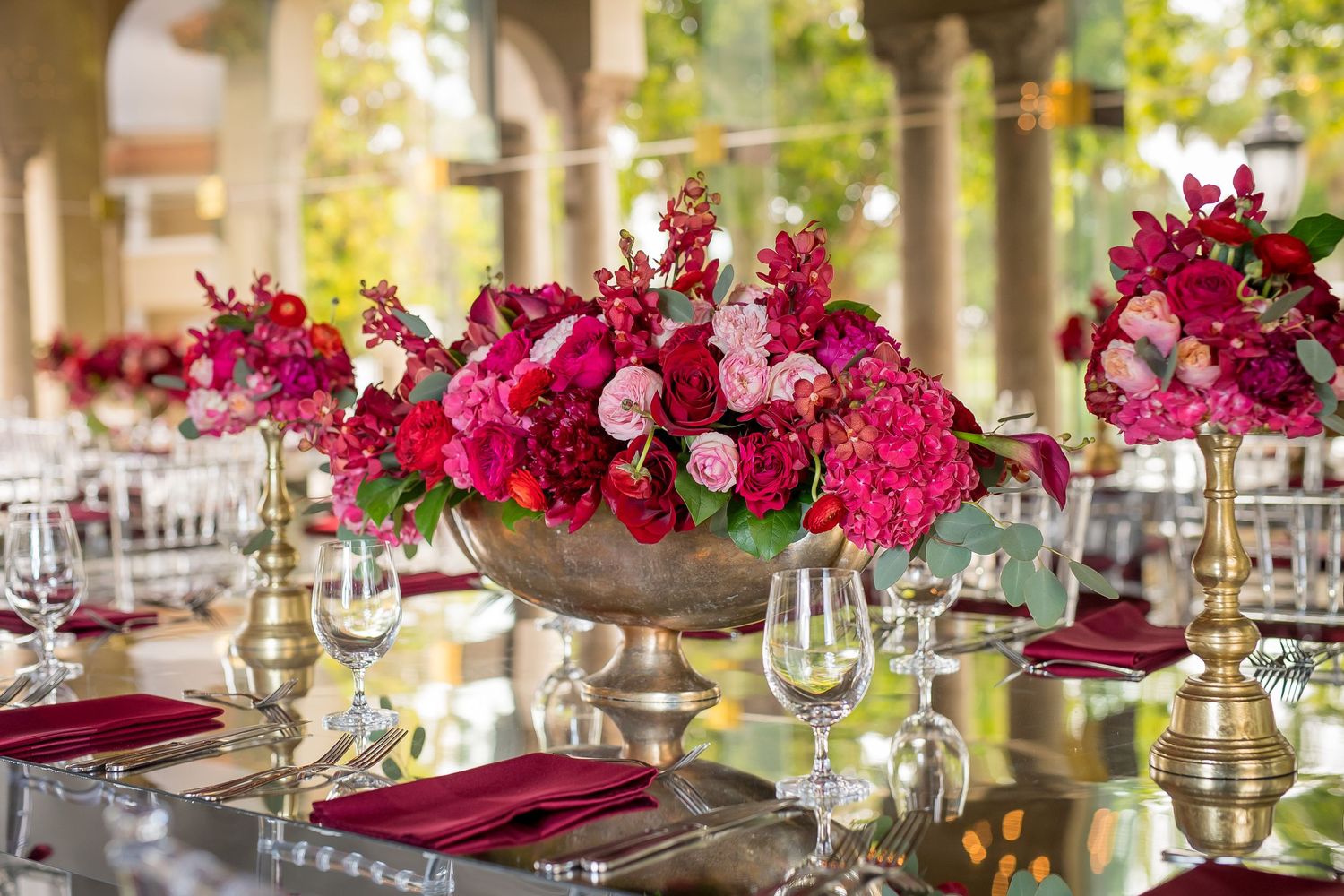 Dramatic burgundy floral centerpiece with gold vase on mirrored wedding reception table.