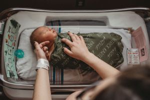 Caring hands tend to a sleeping newborn in a hospital bassinet.