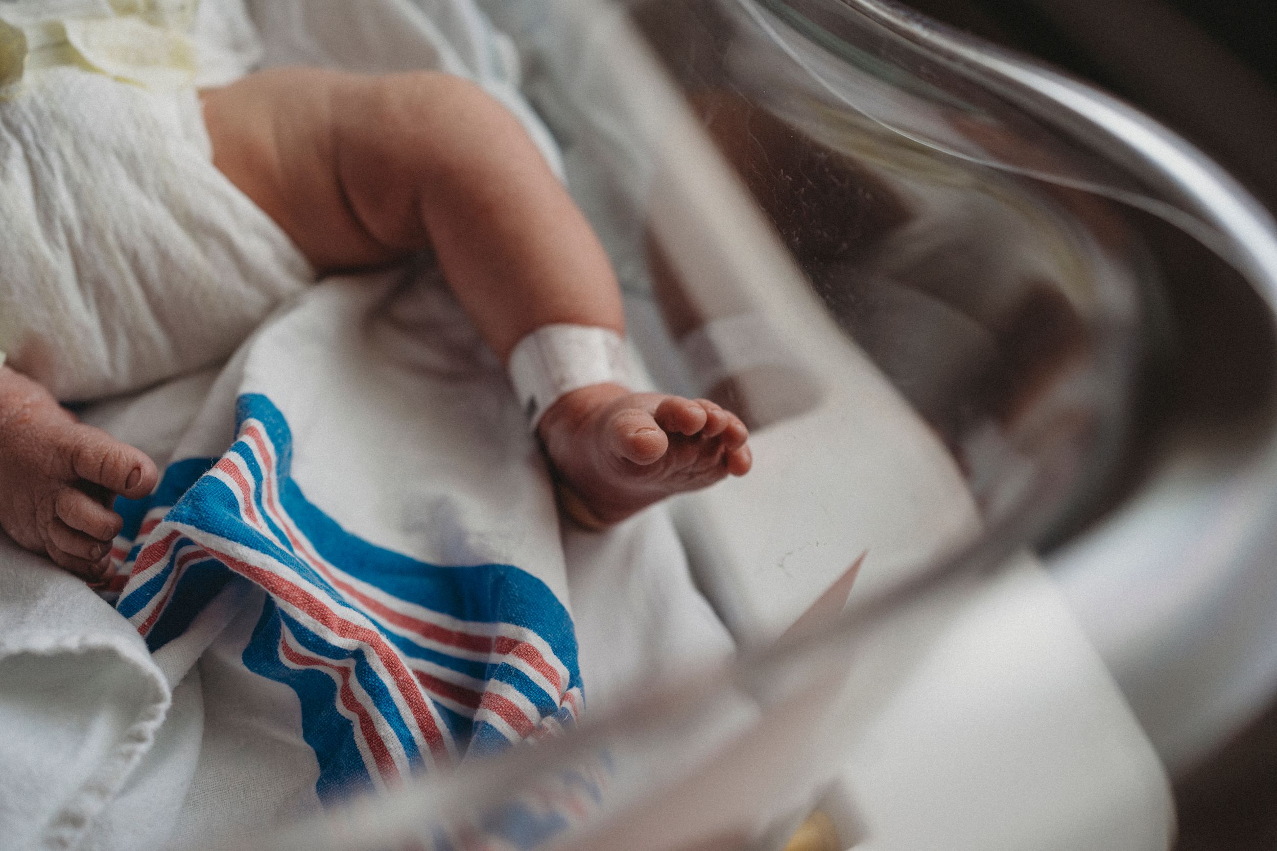 Close-up of tiny baby feet next to a blue and white striped hospital blanket.