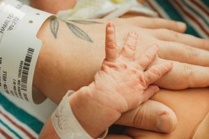 Hospital ID bracelet and tiny newborn hand grasping an adult finger.