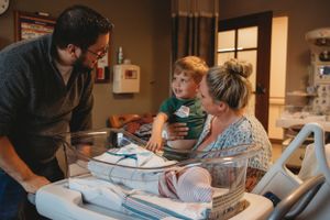 A touching hospital room moment showing a new family gathered around their newborn baby.