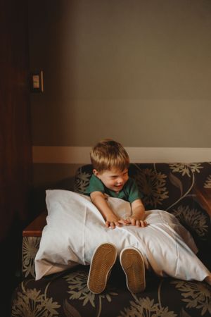 Young child in green shirt playing on a brown patterned couch with a white pillow.