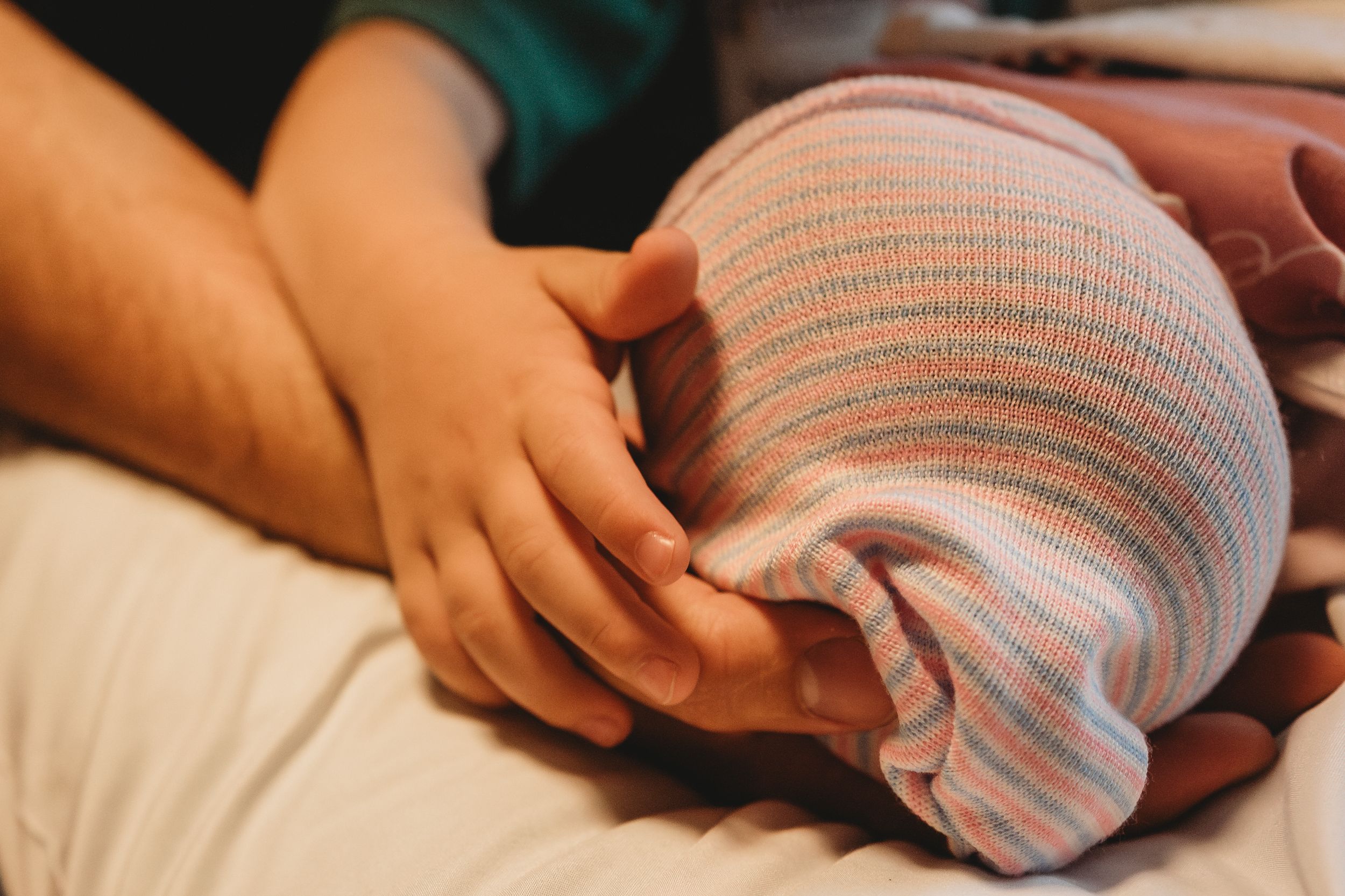 Close-up of small hands gently touching a striped baby blanket.