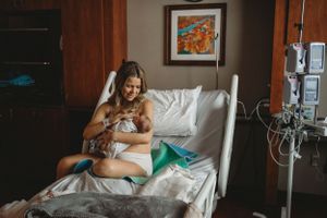 Mother cradles newborn in hospital bed surrounded by medical equipment.